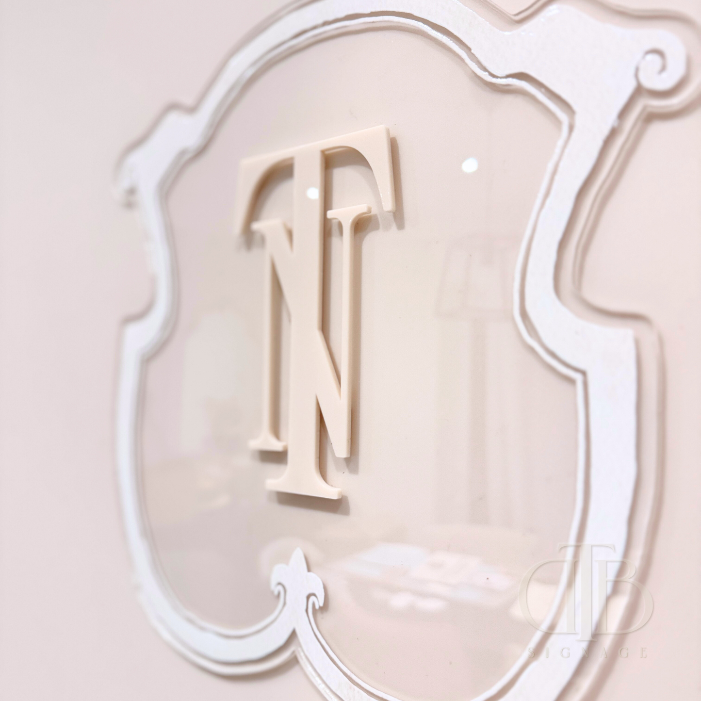 Luxury crest in Beige frame UV printed on clear acrylic, close up view of the initials from left