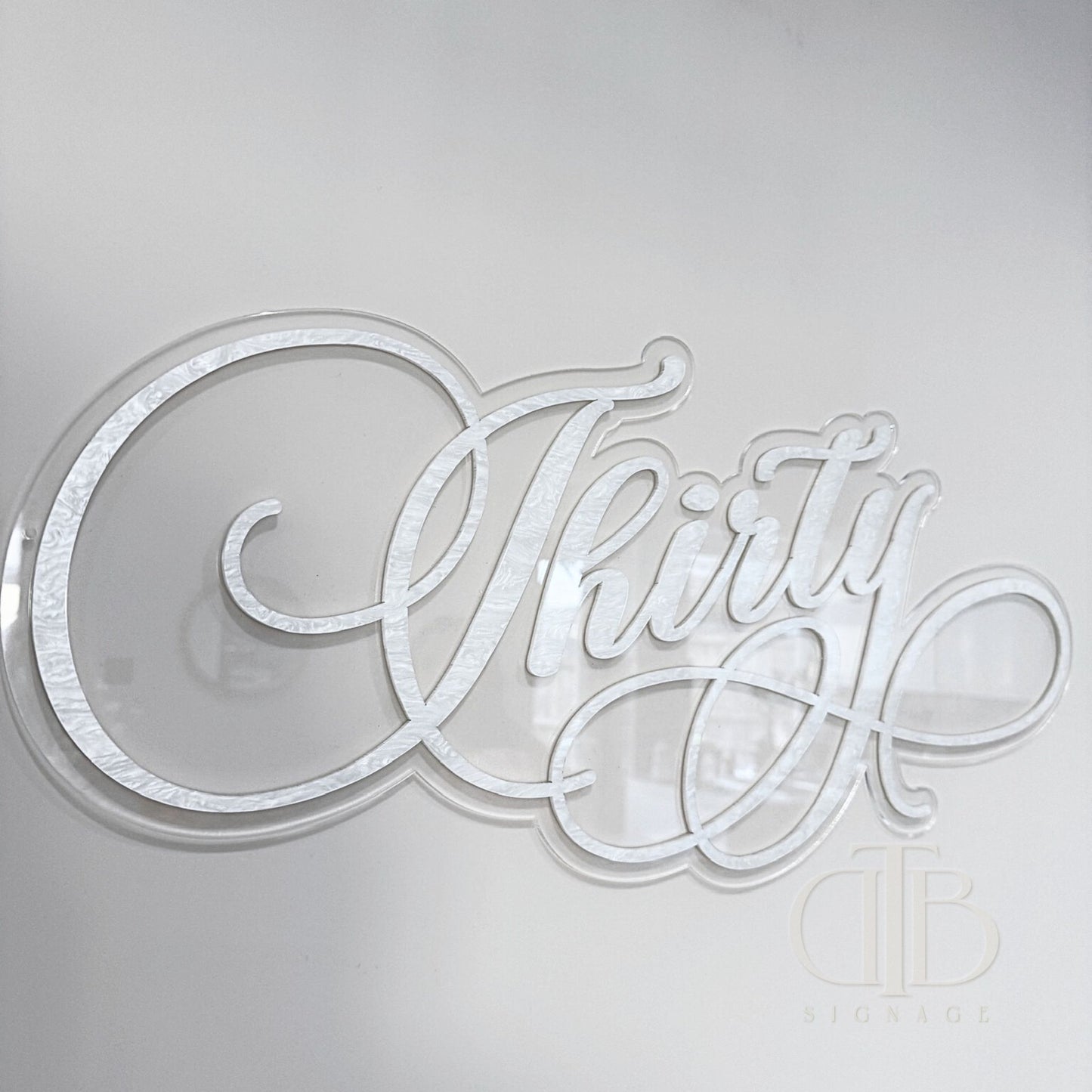 A double layered acrylic sign with the word 'Thirty' written in a cursive script, crafted from pearl acrylic.