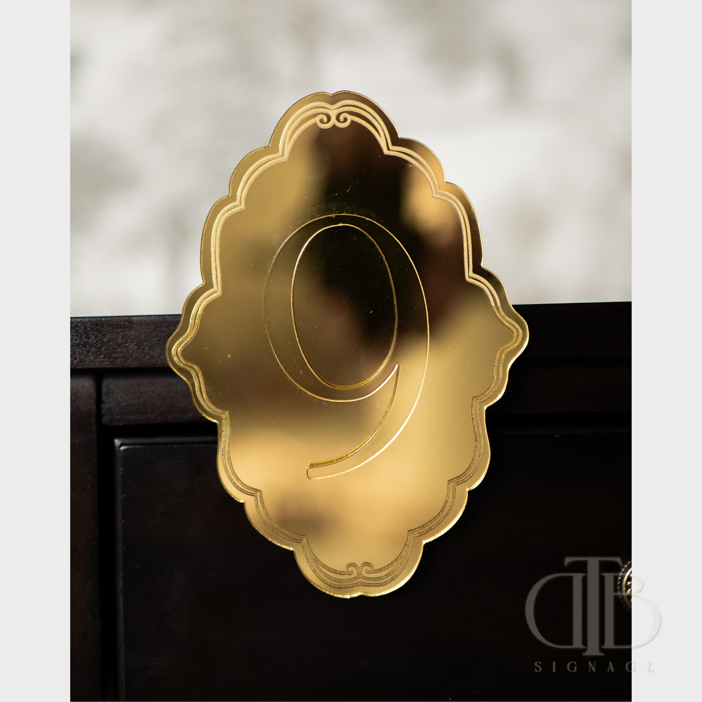 Gold number '9' on a decorative ornate plaque stuck on a table.