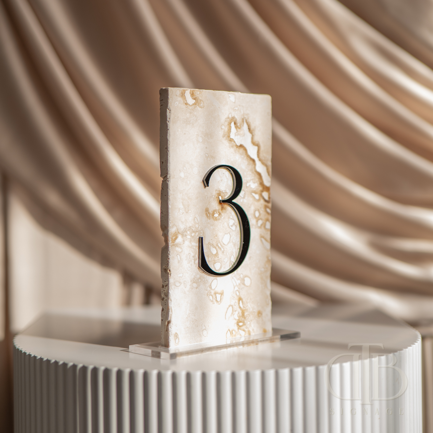 Decorative table number '3' on a marble base with a soft, draped fabric background