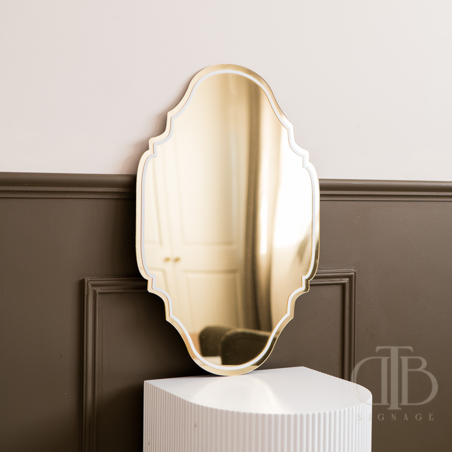 Gold decorative mirror on a white pedestal against a brown paneled wall