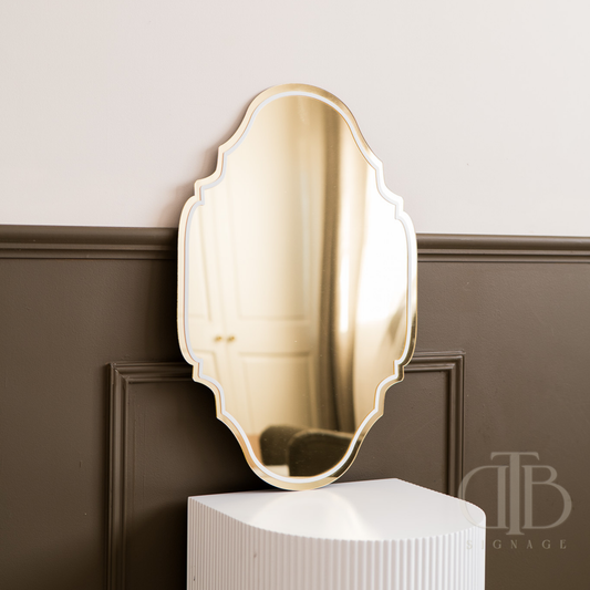 Gold decorative mirror on a white pedestal against a brown paneled wall