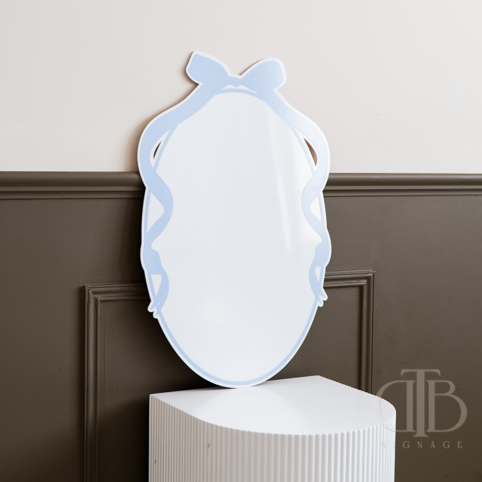 Decorative signage with a blue frame on a white pedestal against a brown wall.