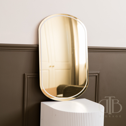 Gold-framed mirror on a white pedestal against a dark wall.