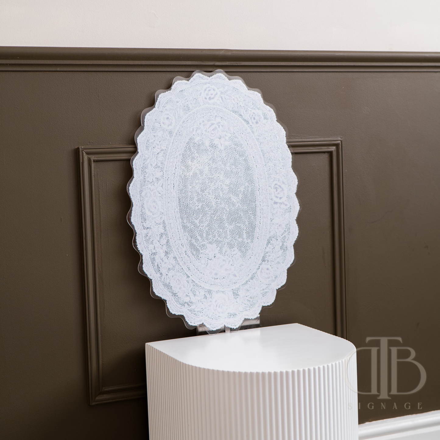 Decorative white lace acrylic signage on a stand against a brown panel wall