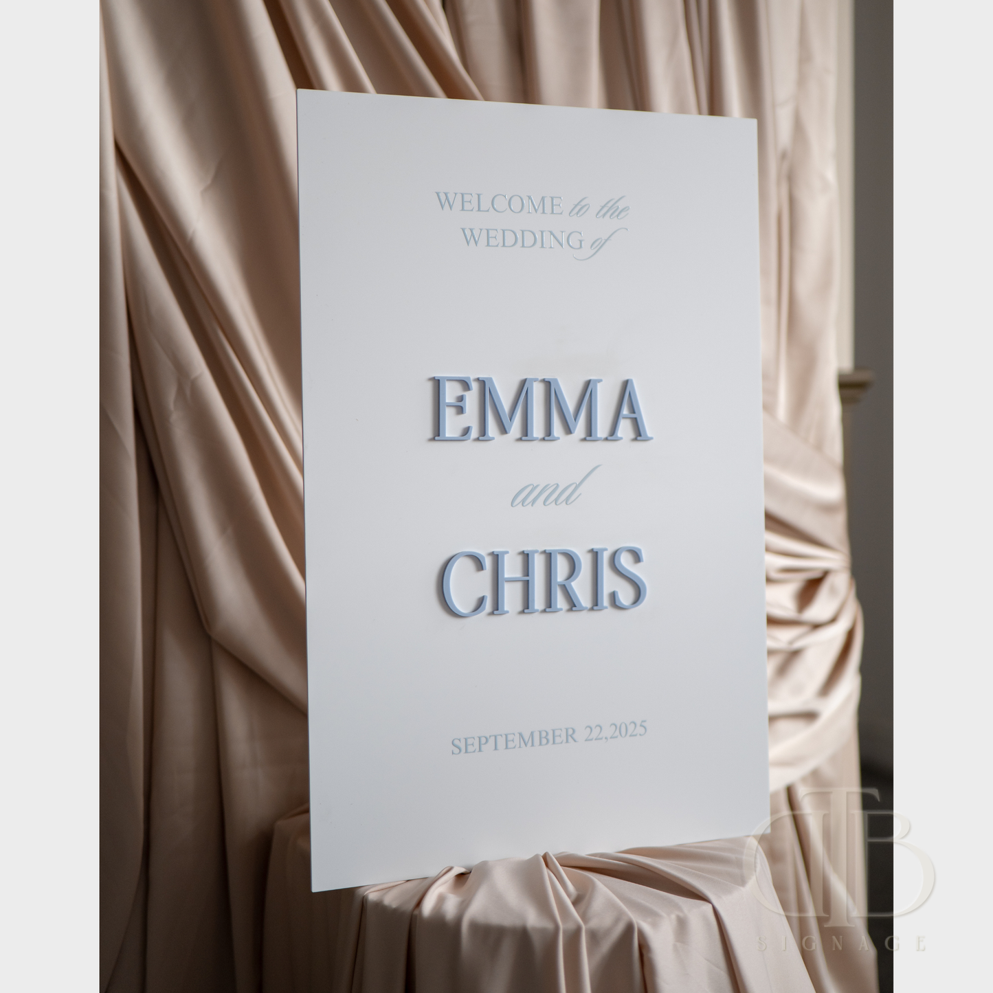 Wedding welcome sign with 'Emma and Chris' text against a draped fabric background