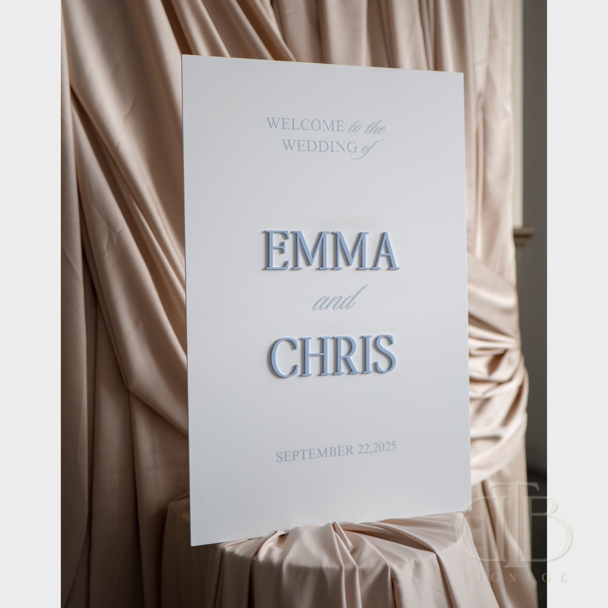 Wedding welcome sign with 'Emma and Chris' text against a draped fabric background