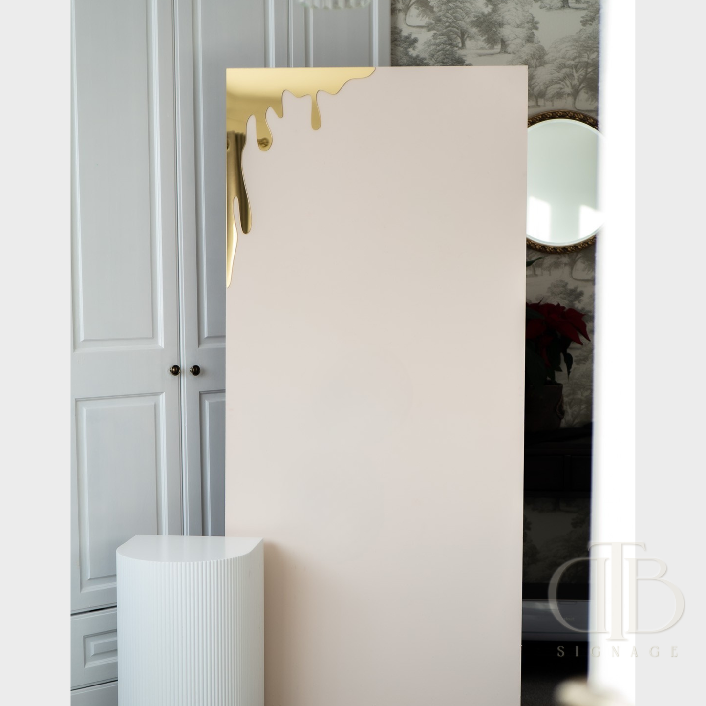 Gold mirror honey drip for Bee theme events leaning against a sailboard in a room with decorative elements.