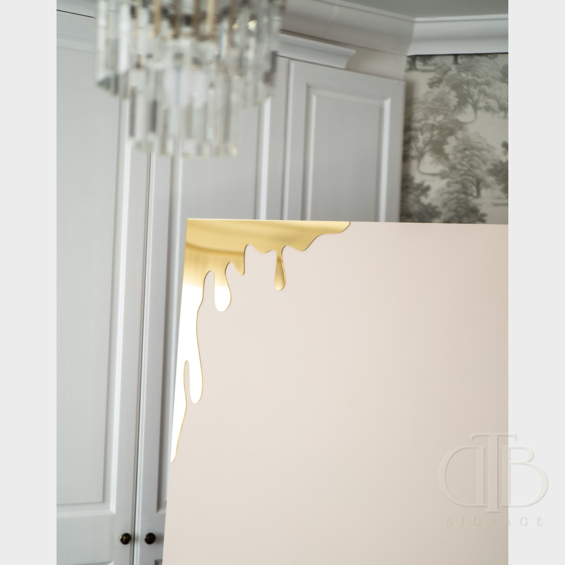 Gold mirror honey drip for Bee theme events leaning against a sailboard in a room with decorative elements.