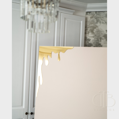 Gold mirror honey drip for Bee theme events leaning against a sailboard in a room with decorative elements.