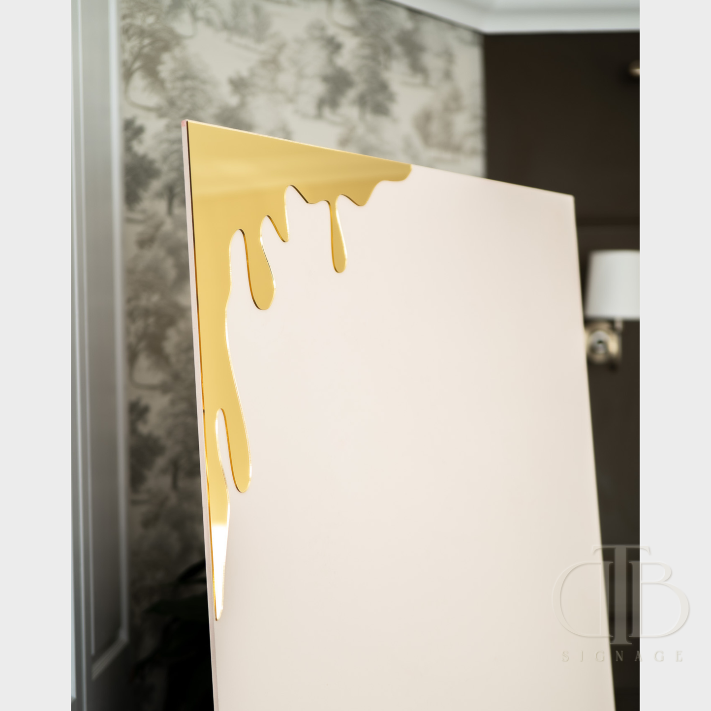 Gold mirror honey drip for Bee theme events leaning against a sailboard in a room with decorative elements.