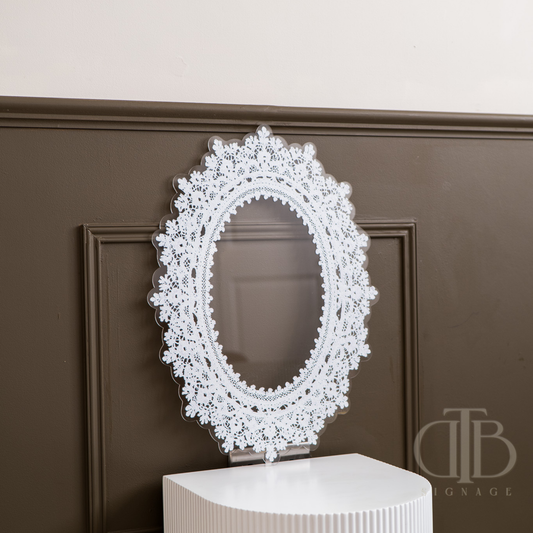 Decorative lace acrylic signage on a white pedestal against a brown wall.