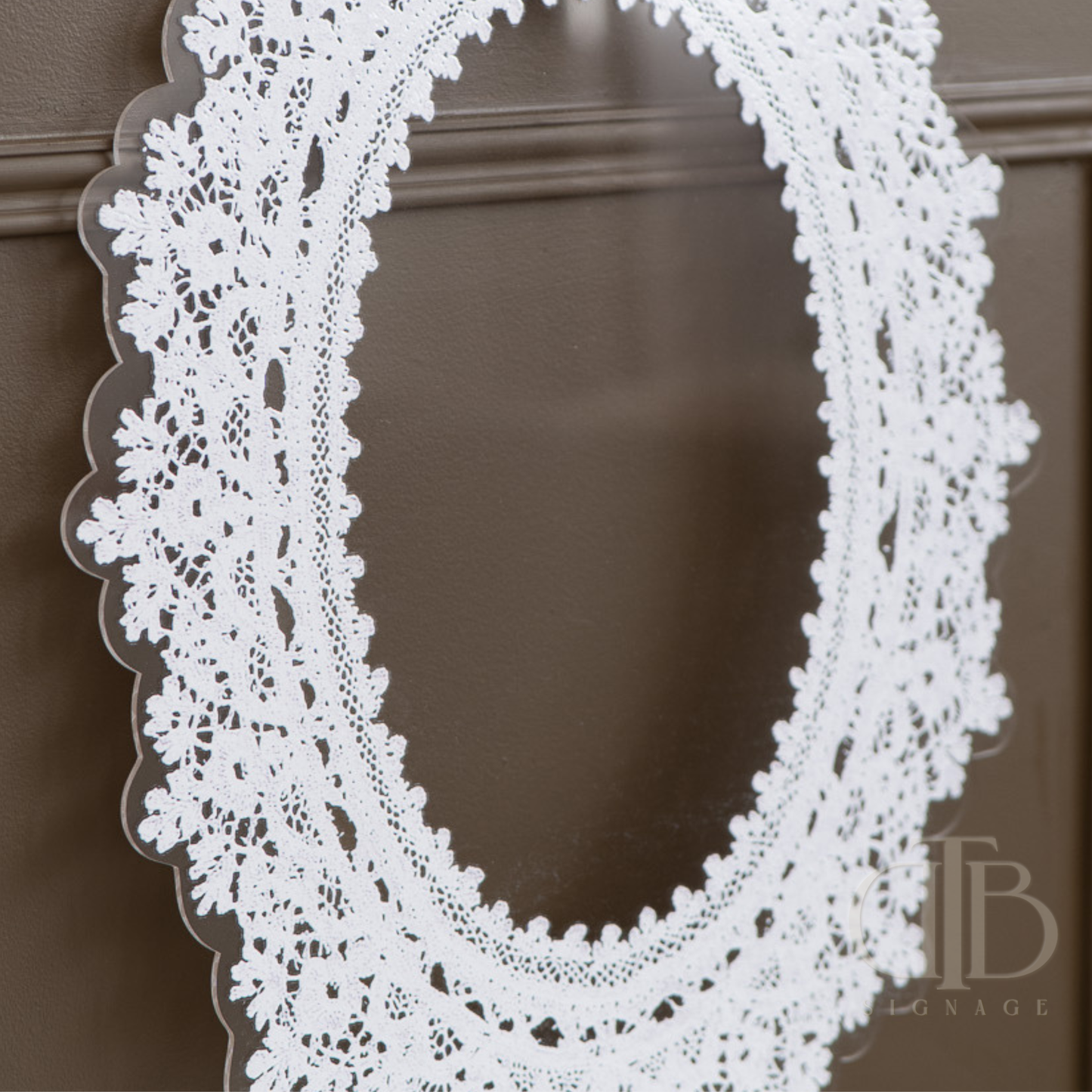 Oval Decorative lace acrylic signage on a white pedestal against a brown wall. with white lace frame on a brown background