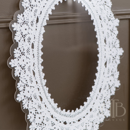 Oval Decorative lace acrylic signage on a white pedestal against a brown wall. with white lace frame on a brown background