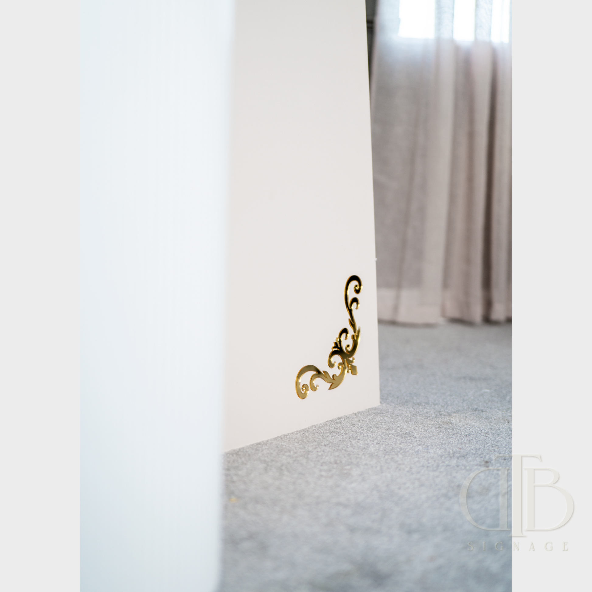Decorative gold wall bracket on a white wall with a blurred room background