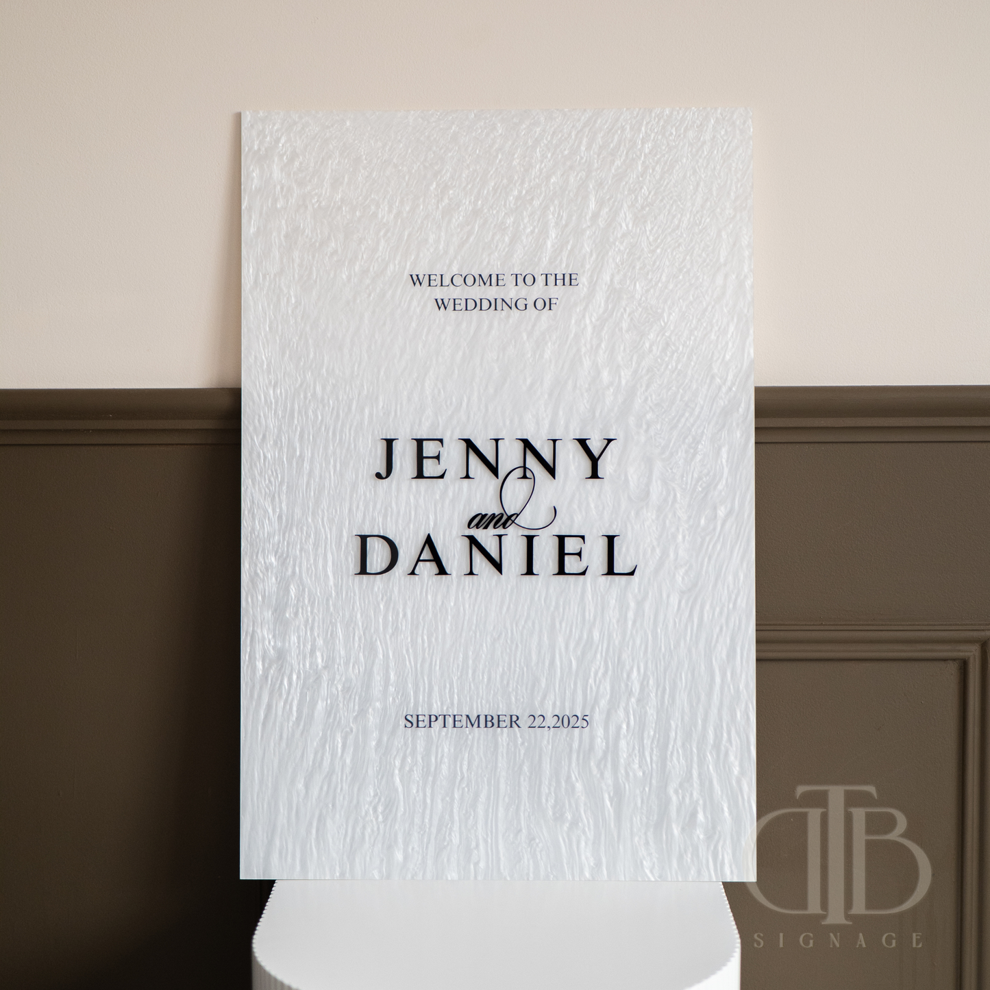 Wedding welcome sign with text 'Welcome to the wedding of Jenny & Daniel' on a textured white background.