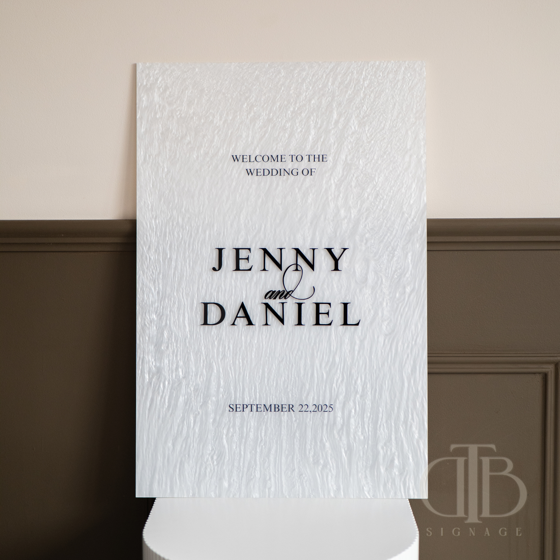 Wedding welcome sign with text 'Welcome to the wedding of Jenny & Daniel' on a textured white background.