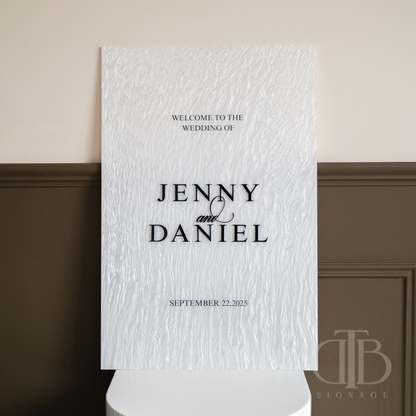 Wedding welcome sign with text 'Welcome to the wedding of Jenny & Daniel' on a textured white background.