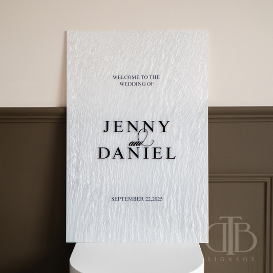 Wedding welcome sign with text 'Welcome to the wedding of Jenny & Daniel' on a textured white background.