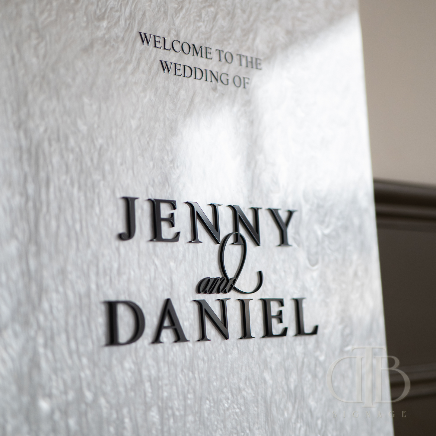Wedding welcome sign with 'Welcome to the wedding of Jenny & Daniel' text on a textured white background.