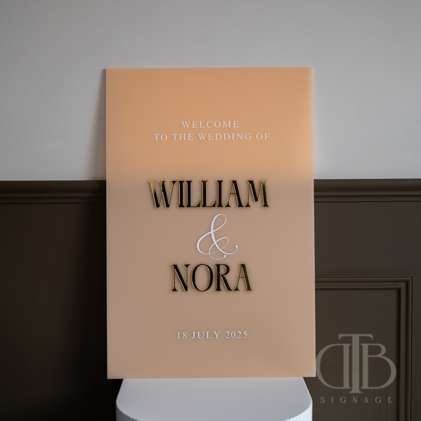 Wedding welcome sign with 'William & Nora' on a stand against a plain background