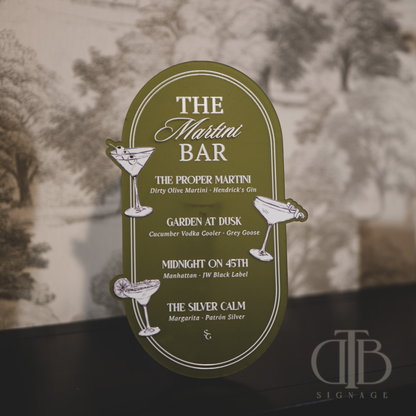 Decorative sign for 'The Martini Bar' with cocktail illustrations and text on a blurred background.