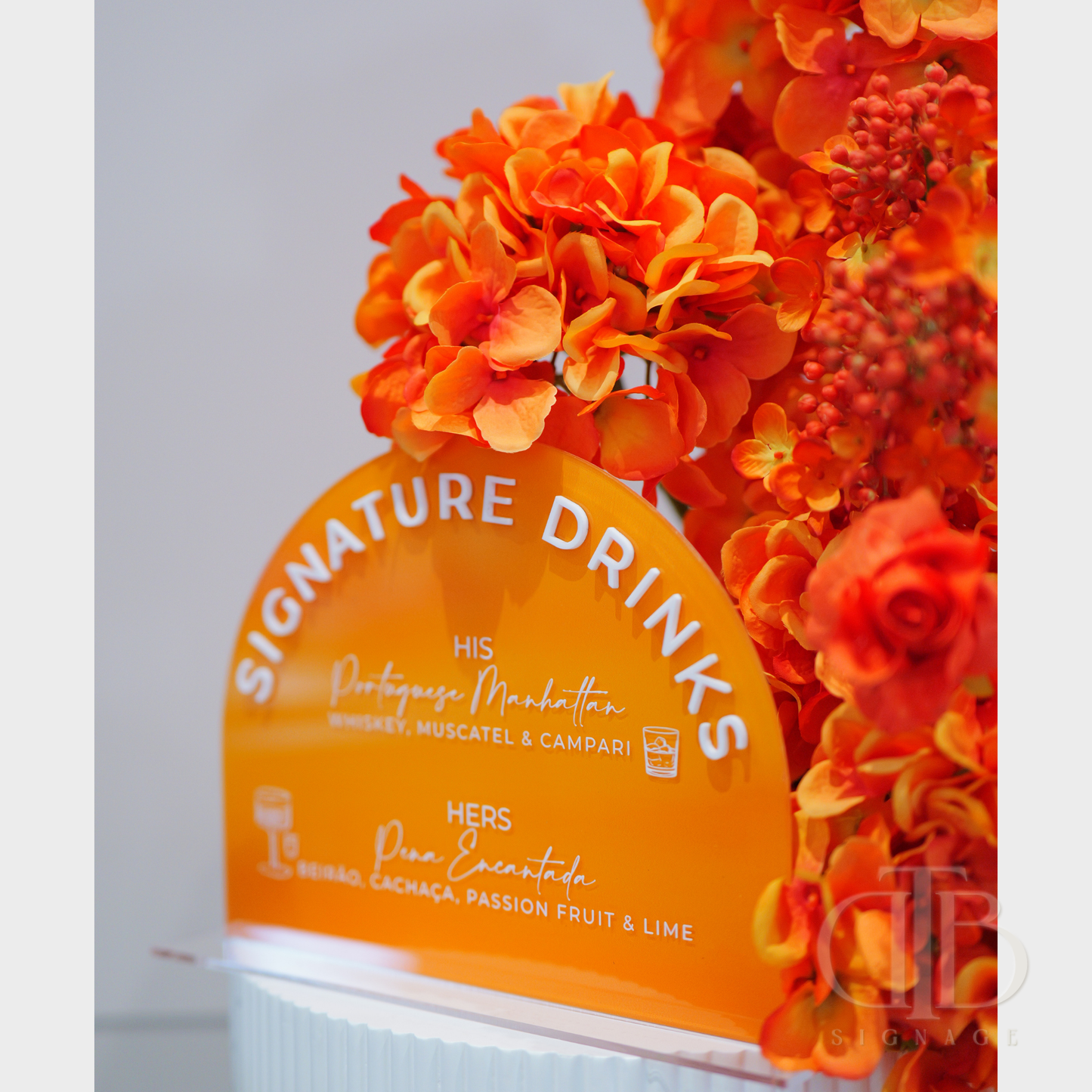 Orange 'Signature Drinks' sign with floral decorations on a light gray background