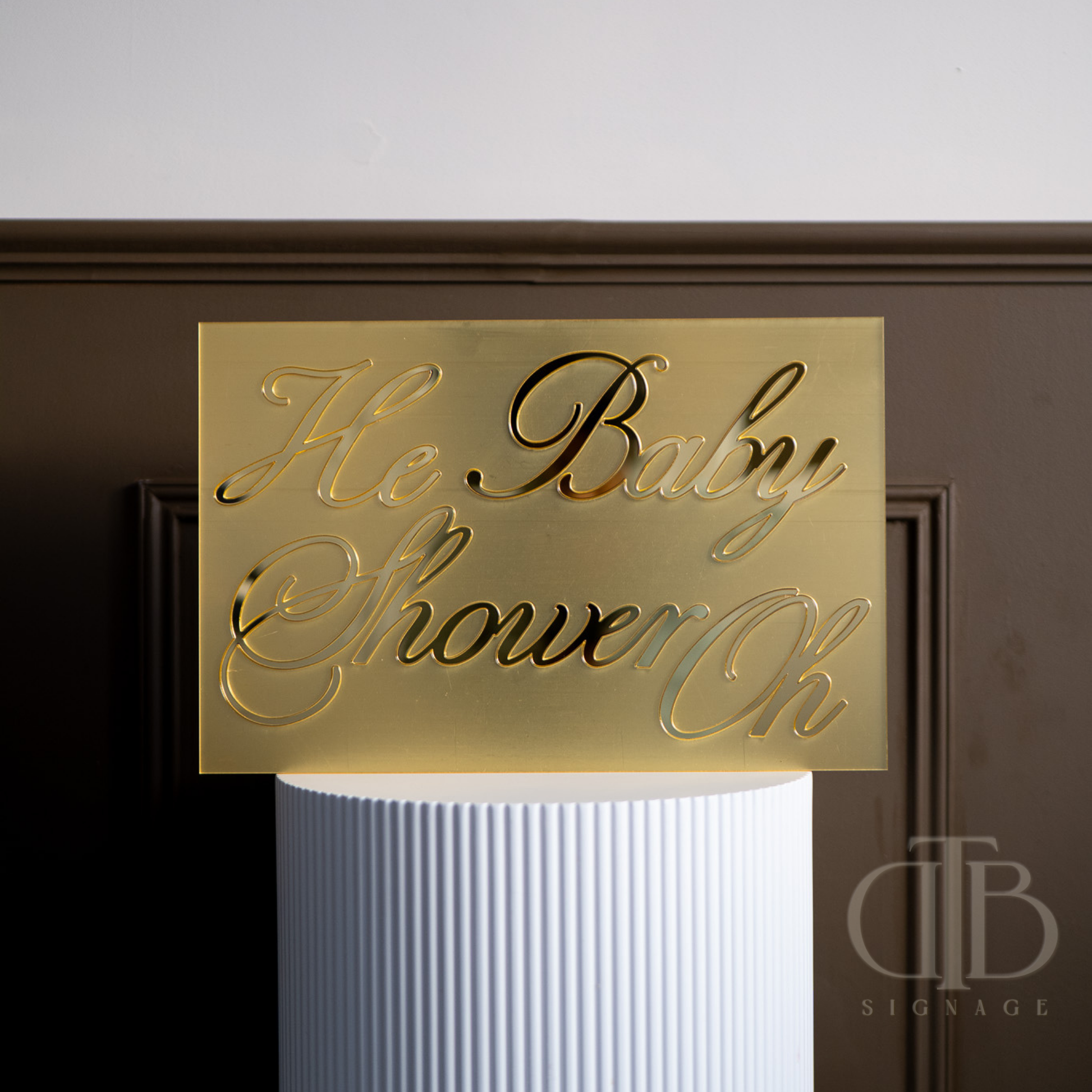 Gold baby shower sign on a white pedestal against a dark background