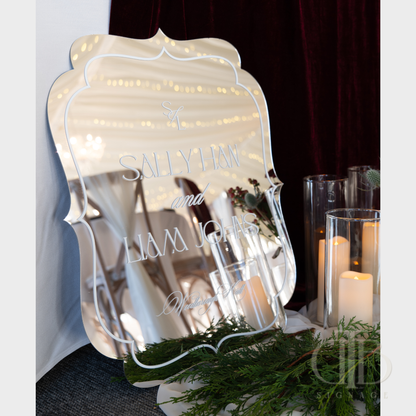 Decorative mirror with personalized text on a table with candles and greenery