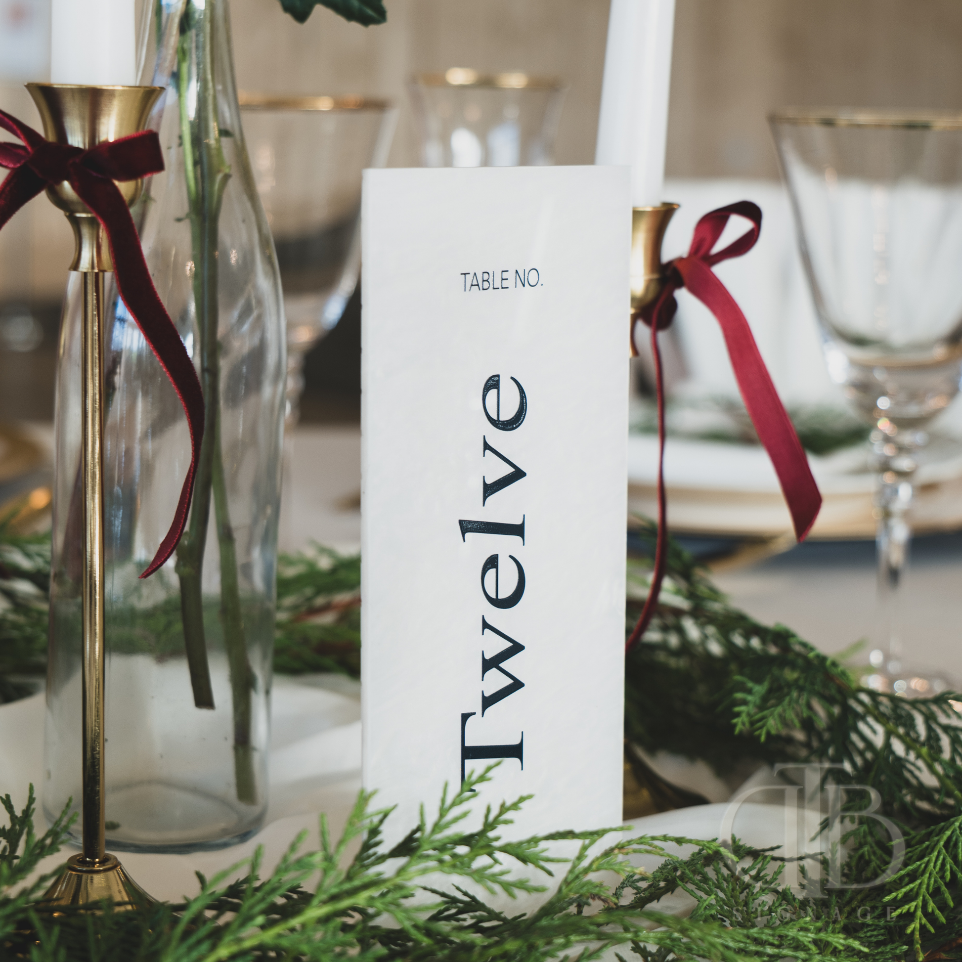 Decorative table setting with a 'Table No. Twelve' card, candles, and greenery.