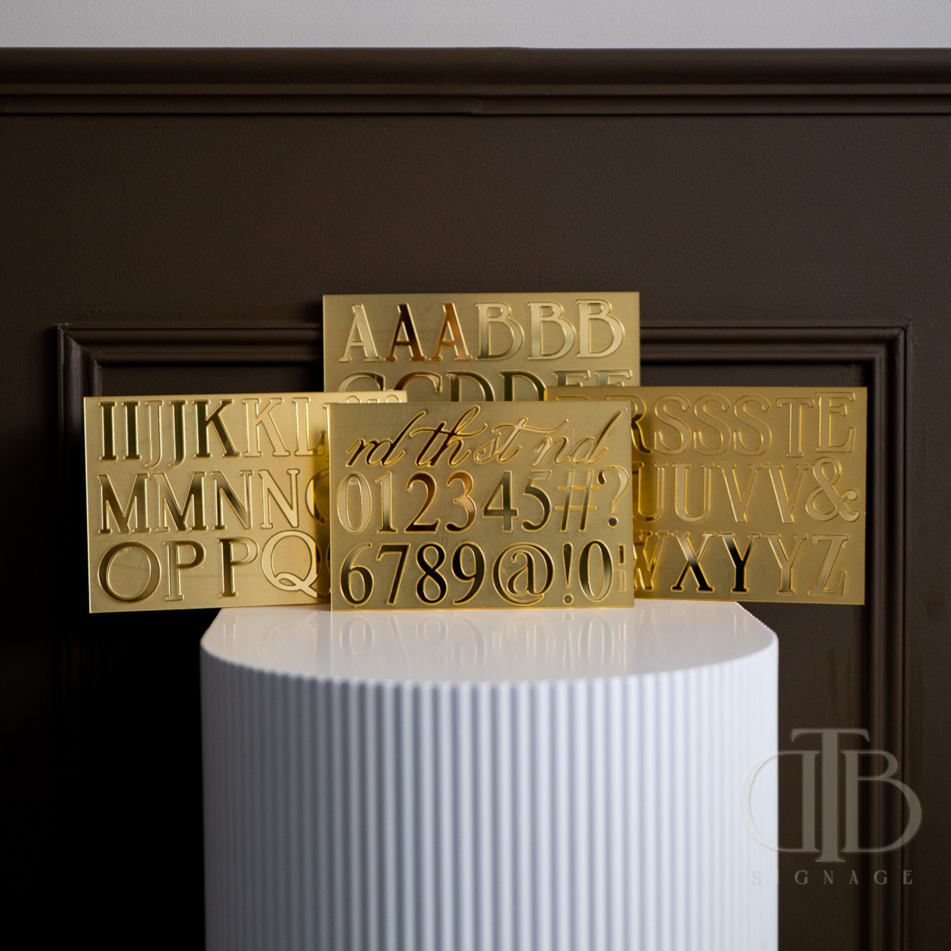 Gold letter and number stamps on a white cylindrical stand against a dark background