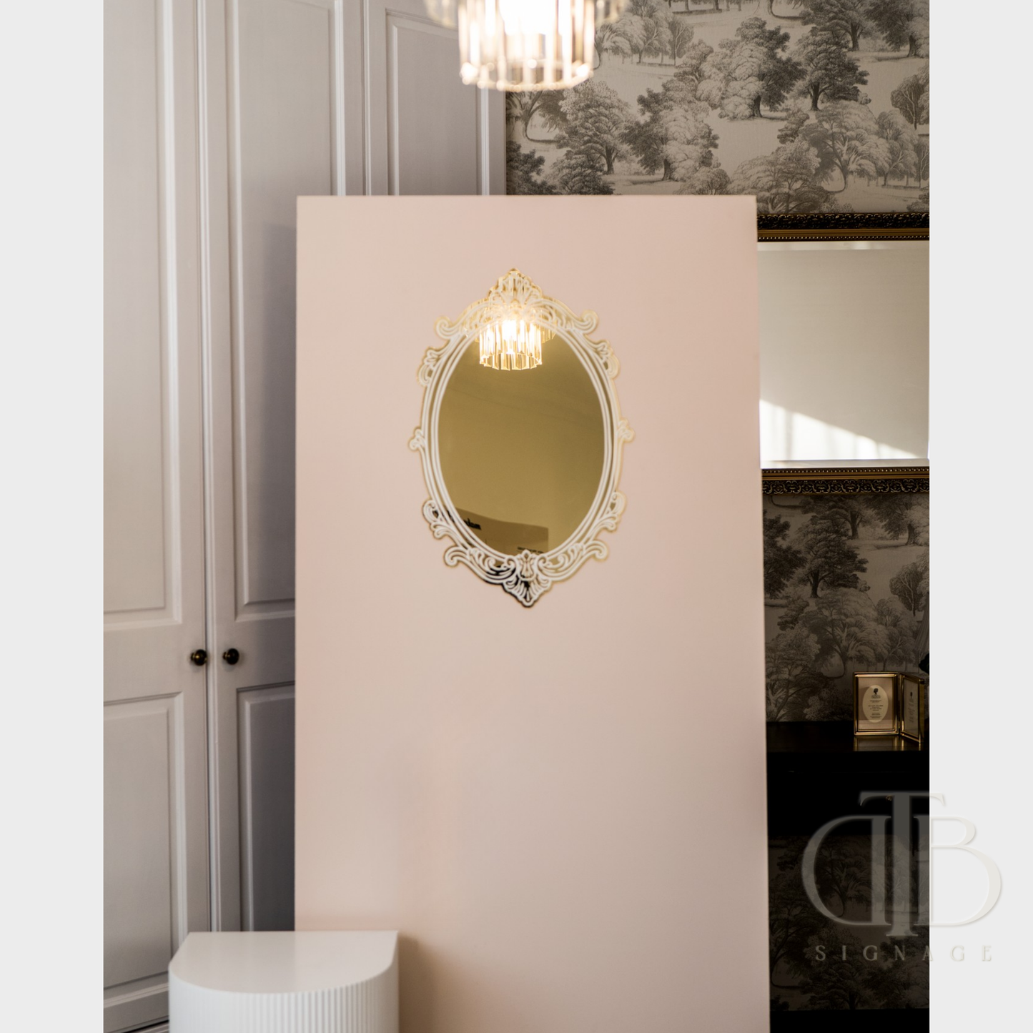 Decorative mirror on a pink wall with a chandelier above