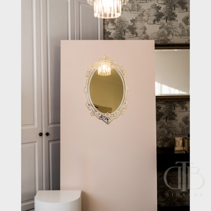 Decorative mirror on a pink wall with a chandelier above