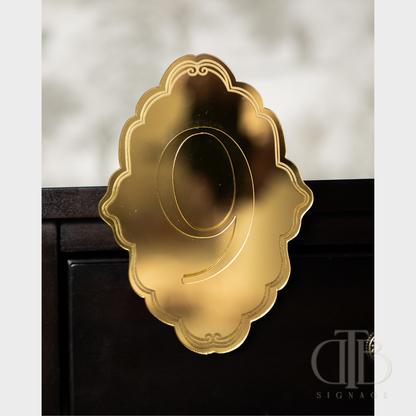 Gold number '9' on a decorative ornate plaque stuck on a table.