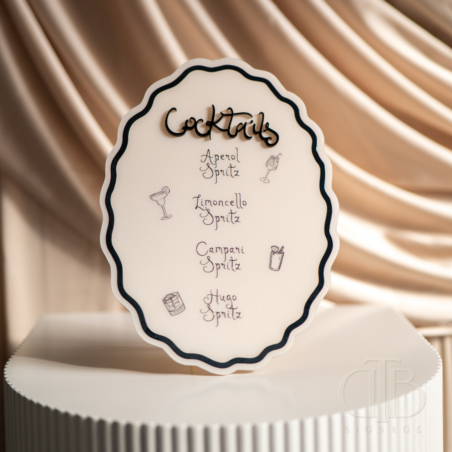 Cocktail menu card on a white stand with a beige draped background
