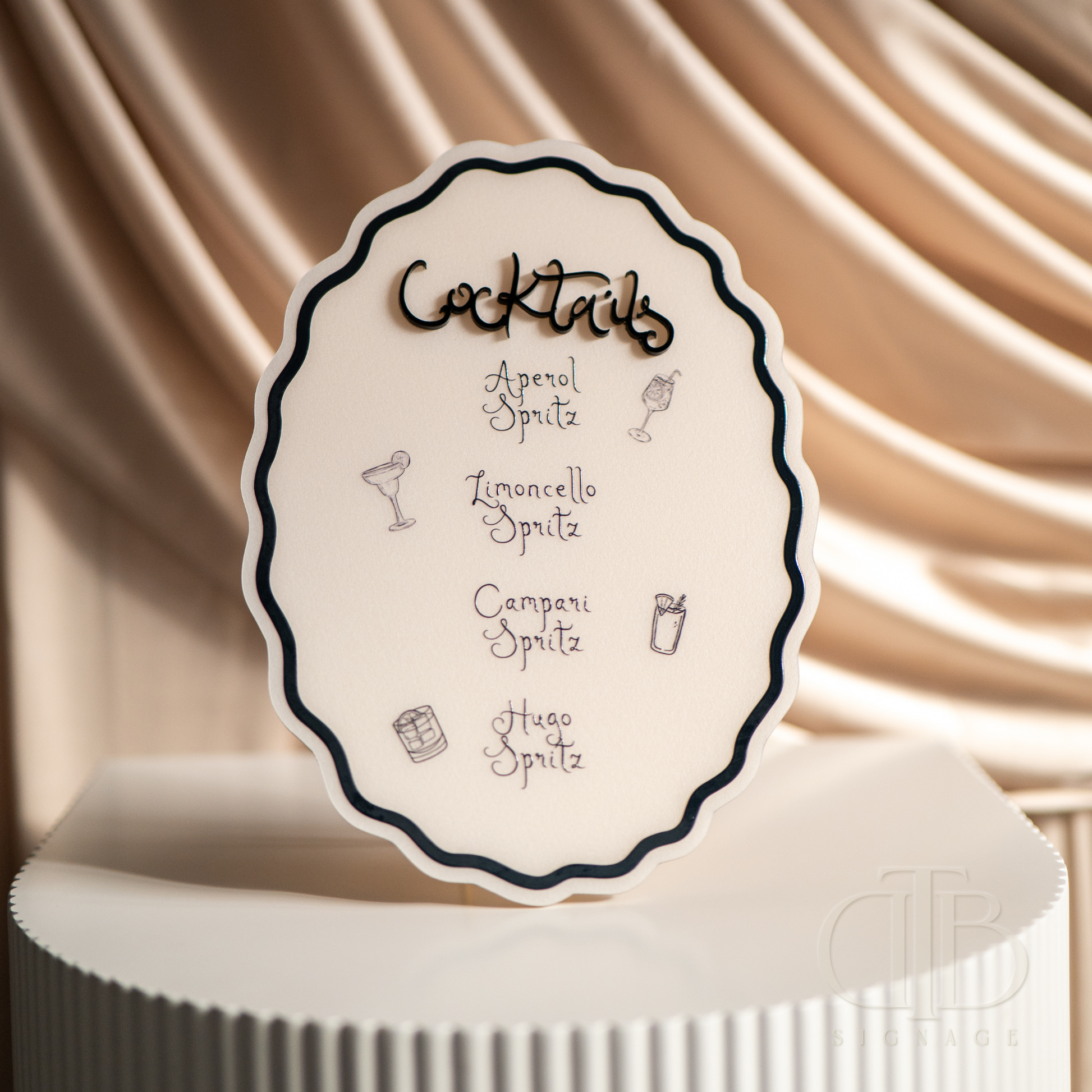 Cocktail menu card on a white stand with a beige draped background