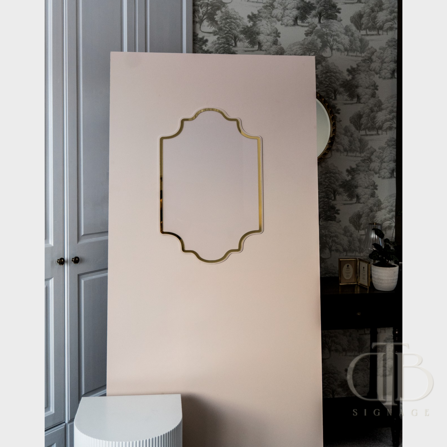 Decorative mirror with gold frame on a beige wall in a room with floral wallpaper.