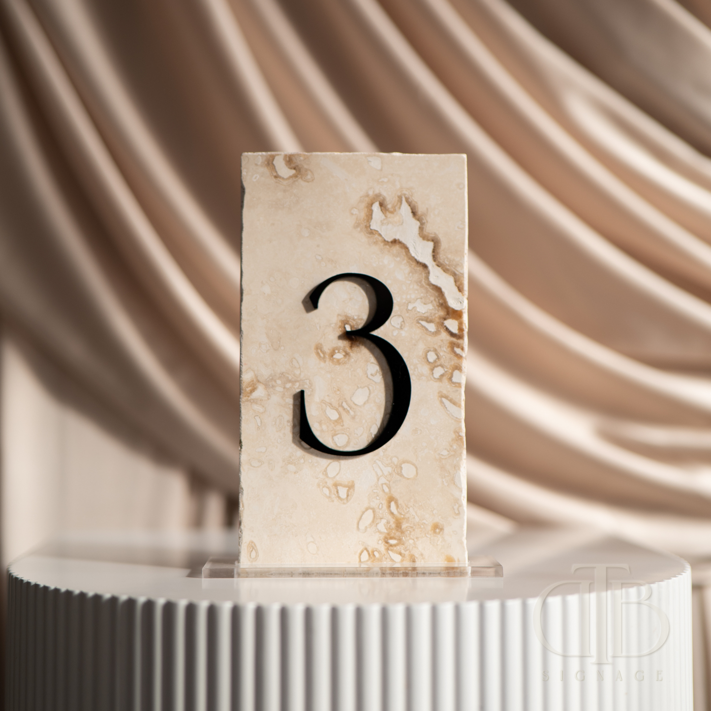 Natural stone table number '3' on a white pedestal with a draped fabric background