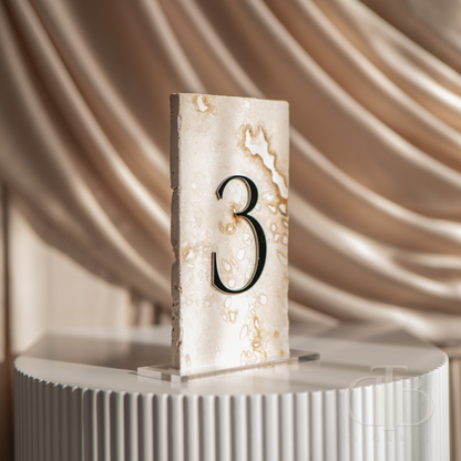 Decorative table number '3' on a marble base with a soft, draped fabric background