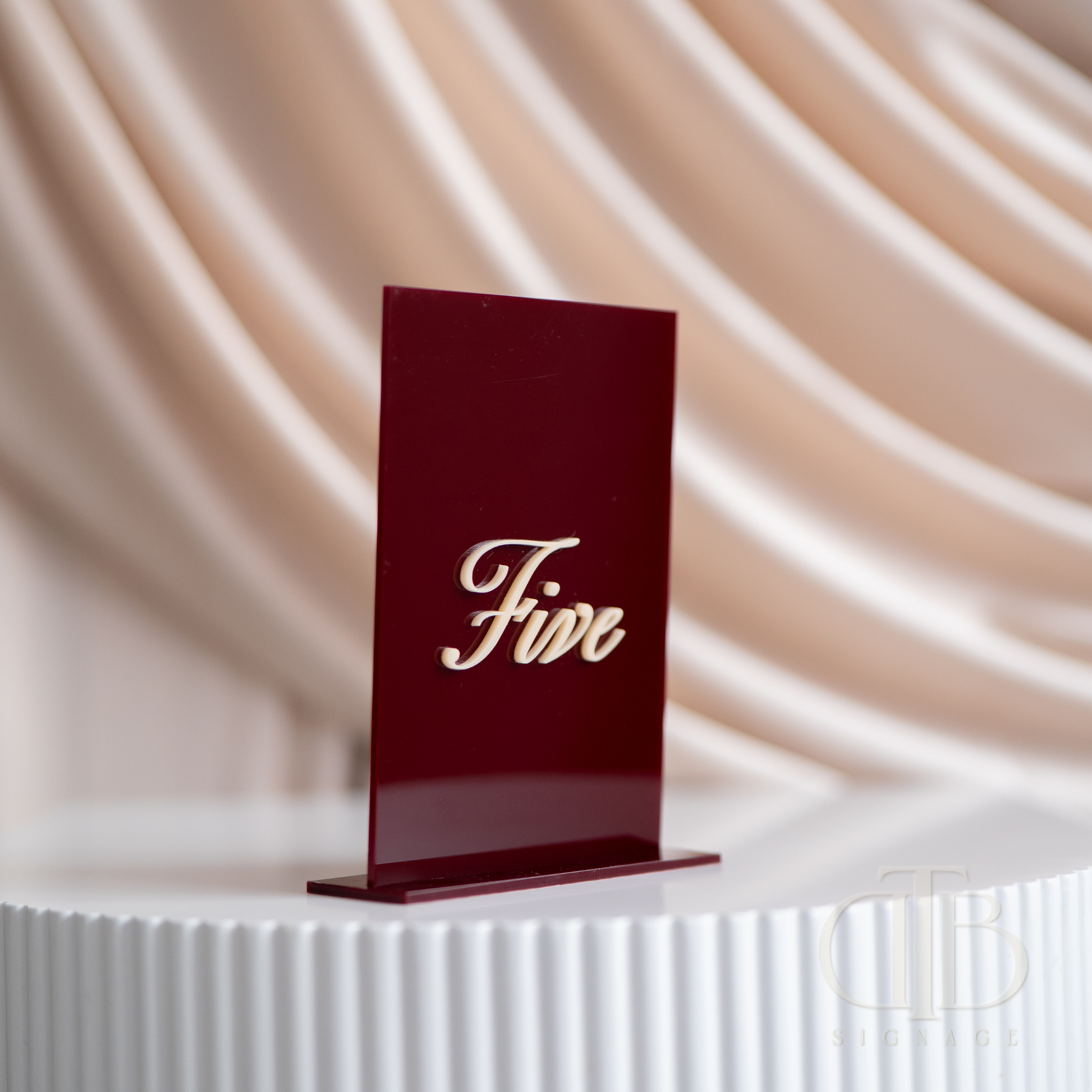 Red card with 'Five' on a white pedestal against a beige curtain background