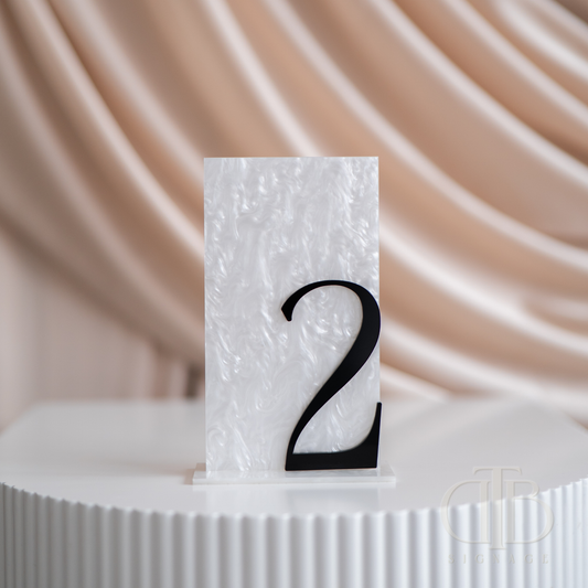 White textured table number card with black '2' on a white surface with a beige draped fabric background.