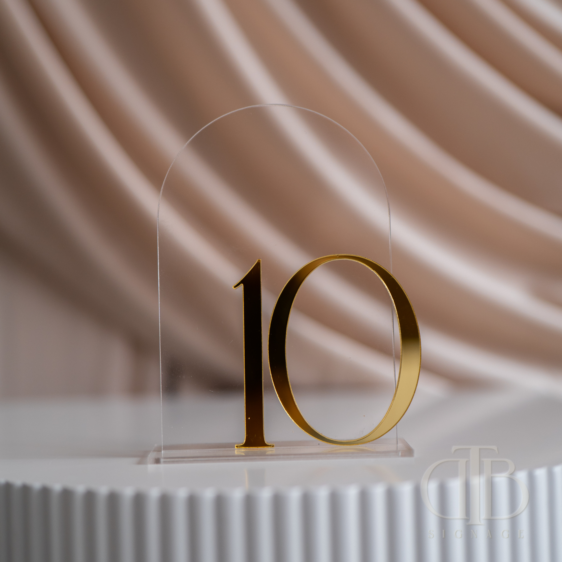 Gold number '10' on a clear acrylic stand against a soft beige background
