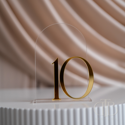 Gold number '10' on a clear acrylic stand against a soft beige background