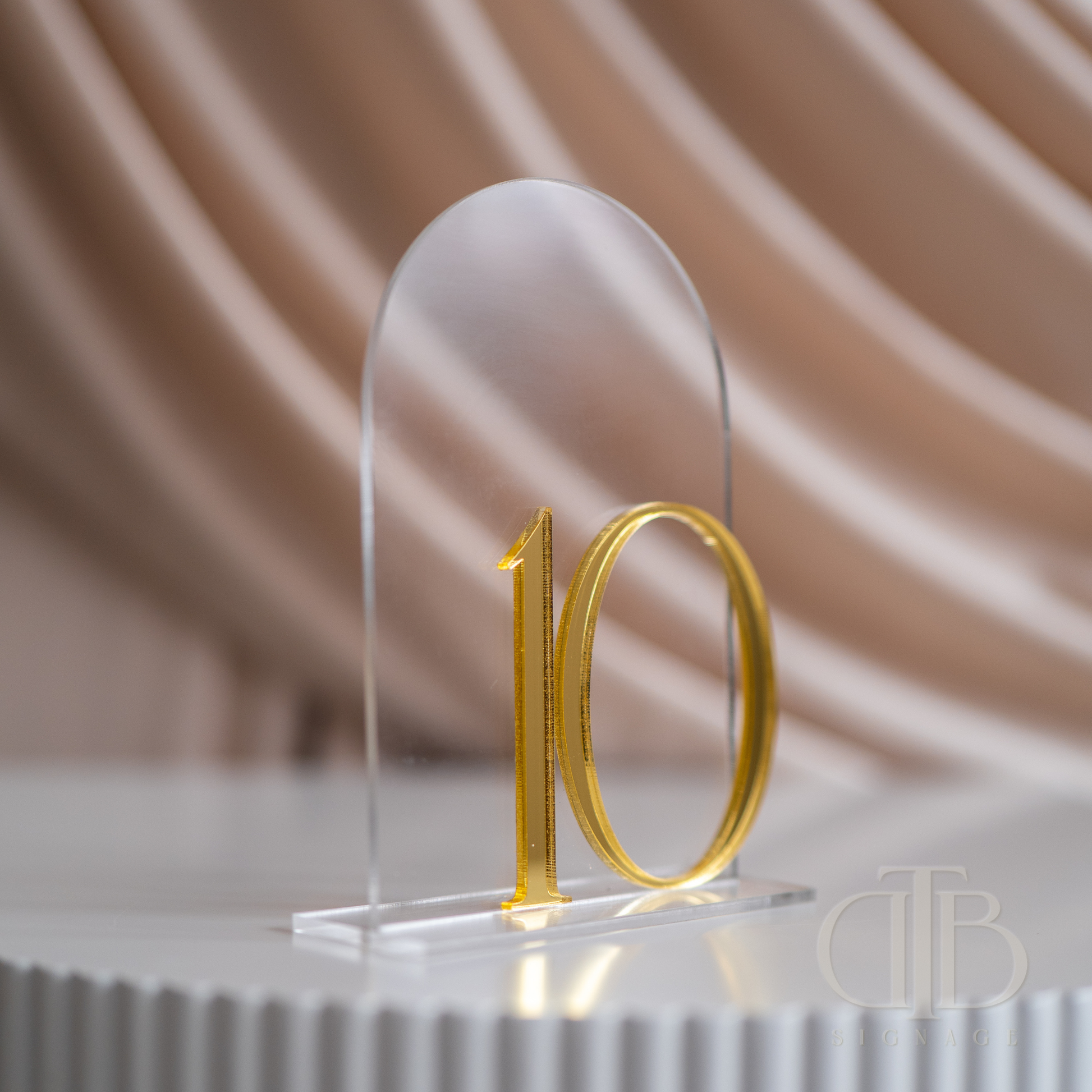 Gold number '10' on a clear acrylic stand with a soft, blurred background