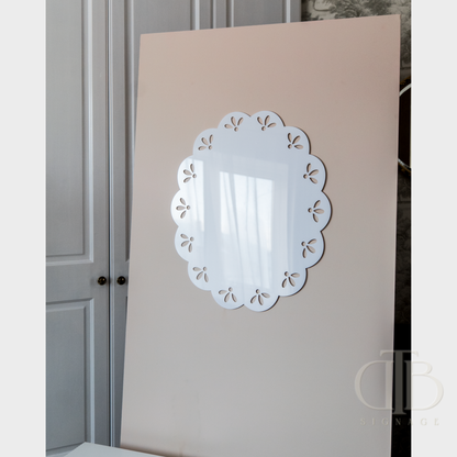Decorative oval acrylic signage with cut-out design on a beige wall.