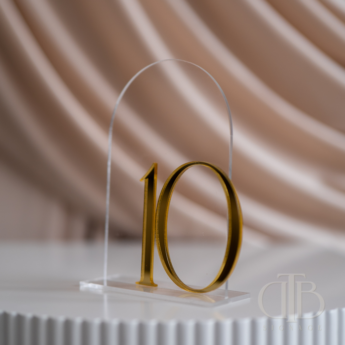 Gold number '10' on a clear stand against a beige curtain background