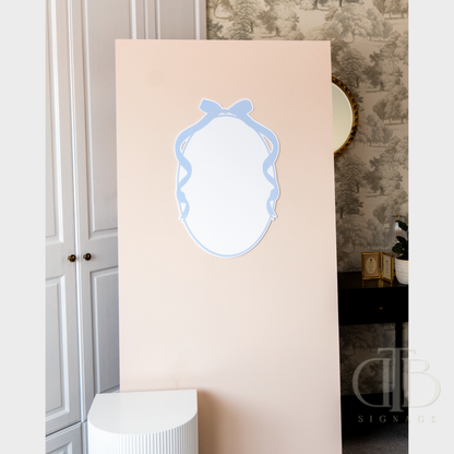 Decorative mirror with blue frame on a beige wall in a room with a textured wallpaper.