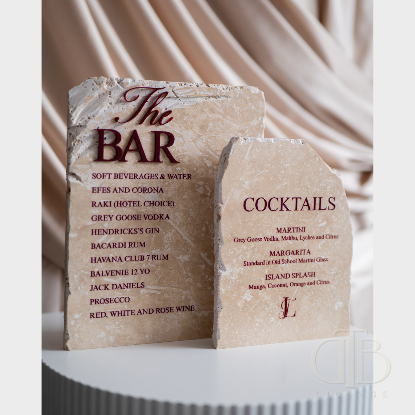 Two stone signs for a bar menu with drinks listed on a draped fabric background.