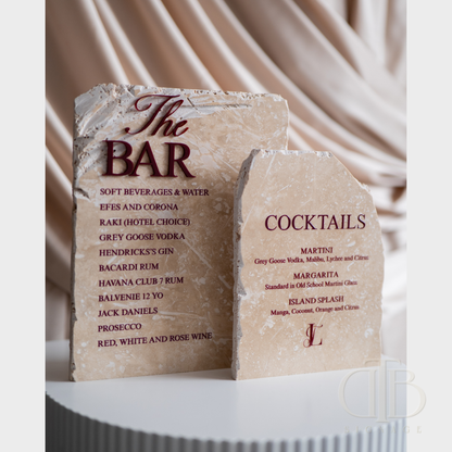 Two stone signs for a bar menu with drinks listed on a draped fabric background.