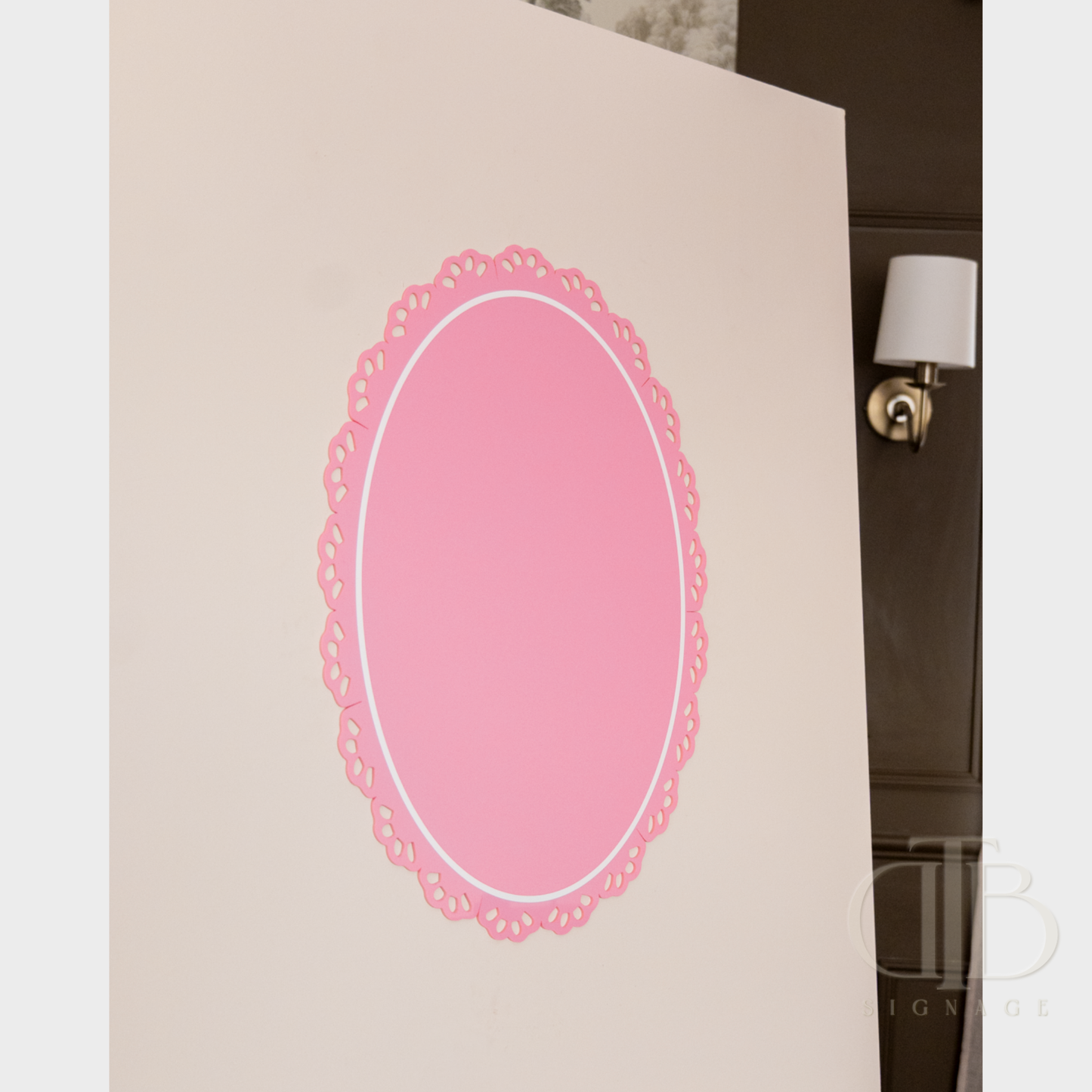 Pink oval acrylic signage with lace edge on a white surface